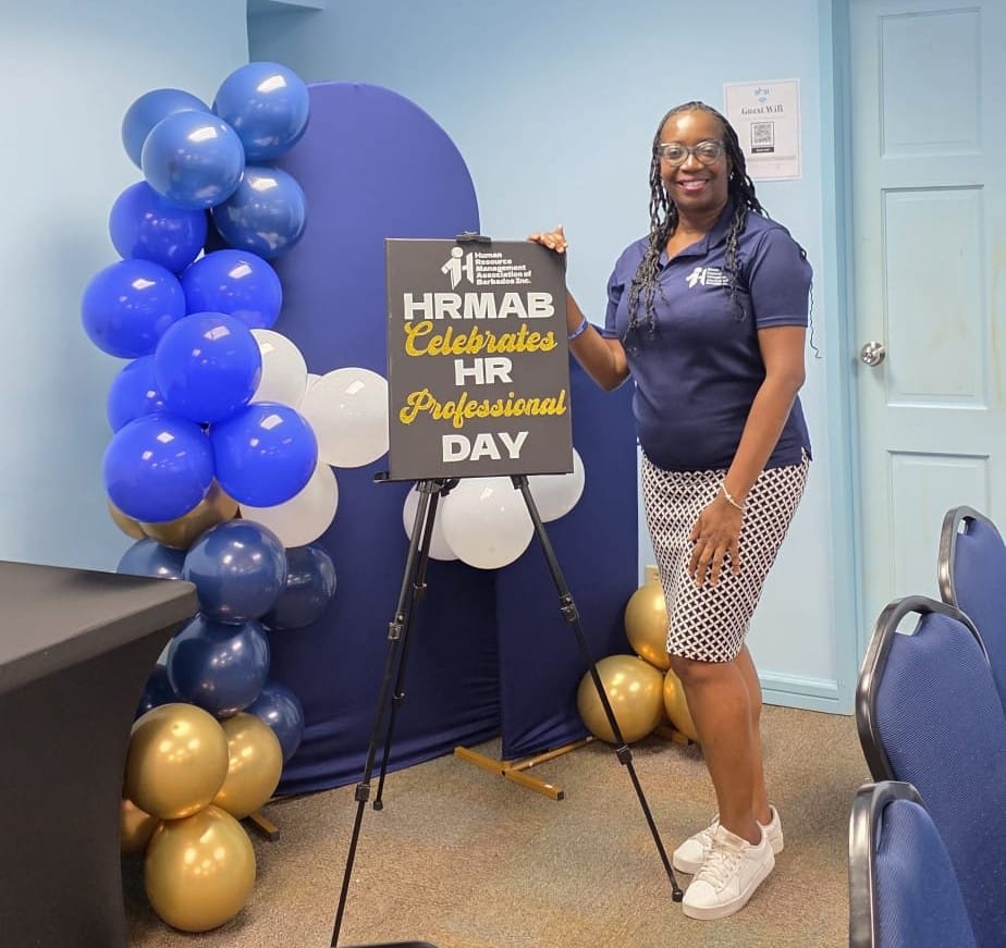 HRMAB team member holding the HRMAB Celebrates HR Professional Day sign beside blue, white and gold balloons